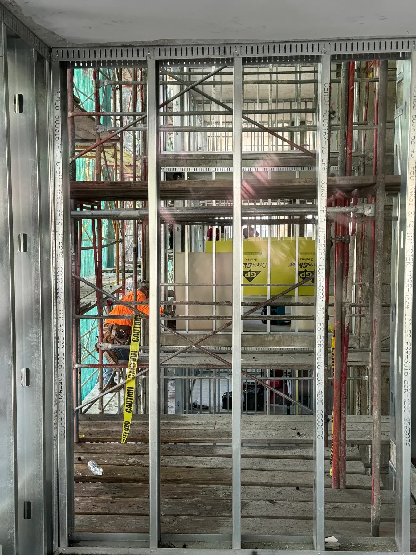 Metal stud wall assembly with exterior sheathing panels going up behind scaffolding