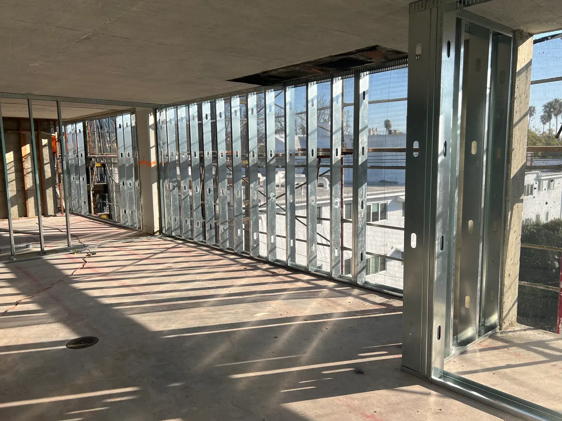 Metal stud window wall framing across a corner of an upper floor, overlooking the surrounding neighborhood