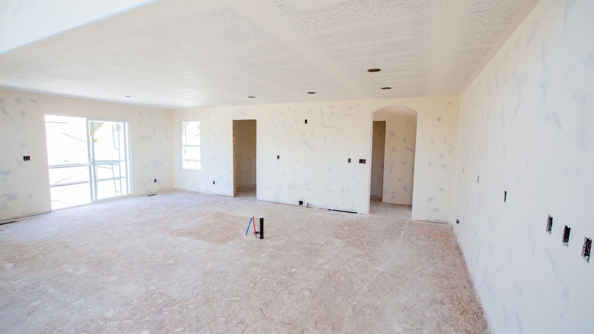 Unfinished interior room with white walls, windows, and construction electrical outlets
