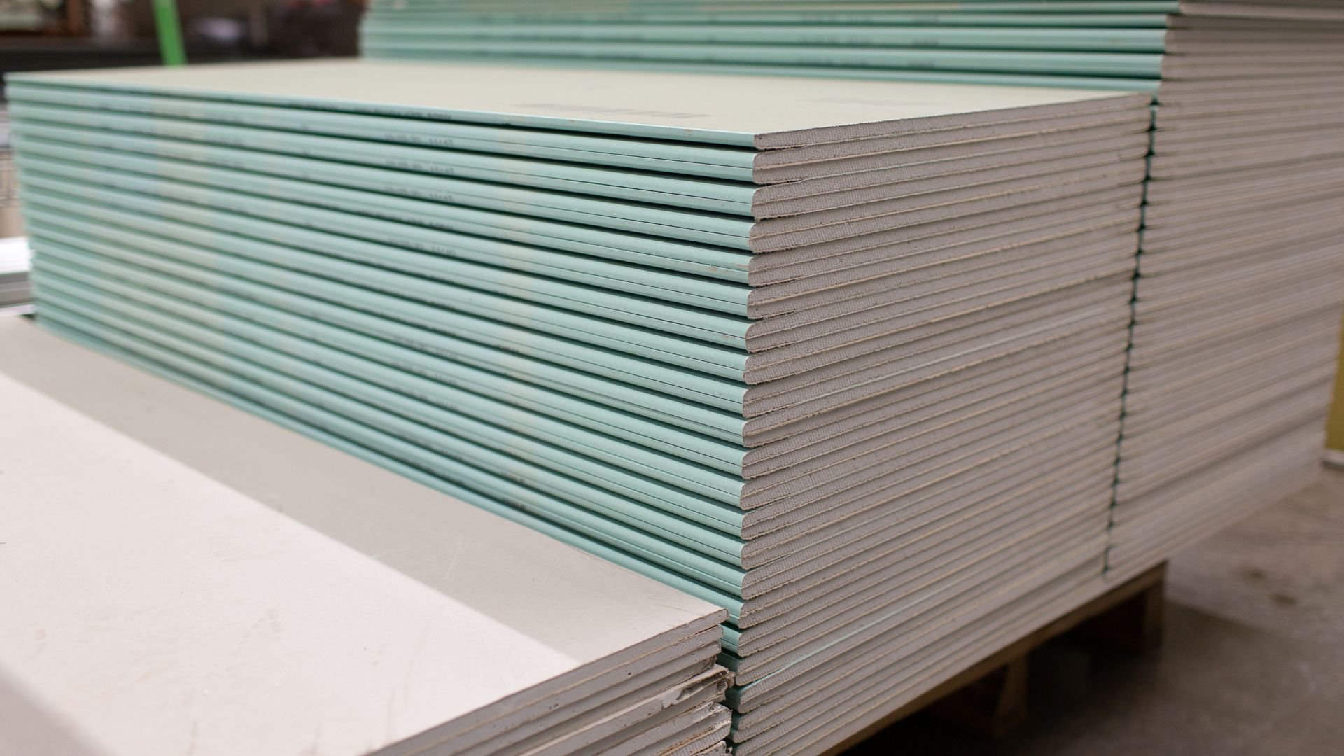 Stacked green and white drywall sheets in a construction warehouse