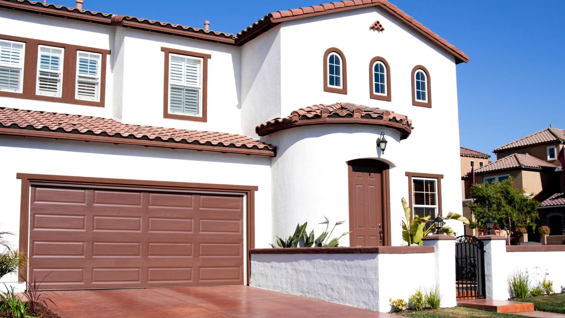 White Spanish-style two-story house with terracotta roof and brown trim