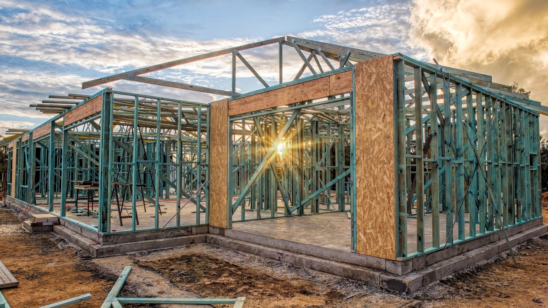 Metal framed house under construction with sunlight streaming through beams